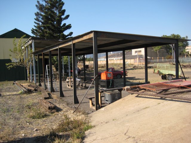 Standing on the platform looking east at the roofed passenger waiting area and the good shed