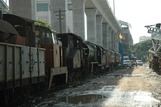 The huge concrete structures of the airport rail link tower over the line of dumped locomotives of the SRT, near Makassan workshops, Bangkok. The overhead station building can also be seen, as the link approaches the Pratunahm district, where many of the popular hotels are located