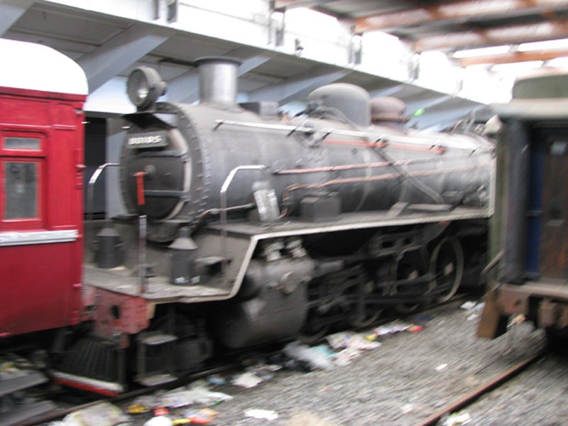 An American looking locomotive standing inbetween coaches near all the other ones. Also note the rubble that somebody is just dumping onto the tracks