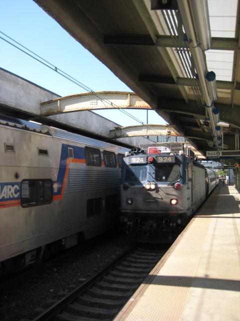 An electric loco hauls New York-bound regional train 147 into Baltimore, Maryland, with a double-decker suburban train standing in the adjacent road