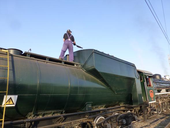 Nathan tries a new firing technique, standing on the tender instead of the footplate. Actually he is trimming coal, ie moving coal from the rear of the bunker to the front where it can easily be reached by the fireman during the journey