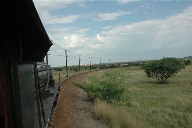 The Tshwane Xplorer really travels mostly through suburbia, except for one section near Pyramid South. Yet, we cannot escape progress, and in the distance the cluster of buildings of the national roads Petroport breaks the bushveld scene, as the train enters the balloon of the marshalling yard.<br />Motorists on the highway will now witness the spectacle of steampower so<br />near to them.