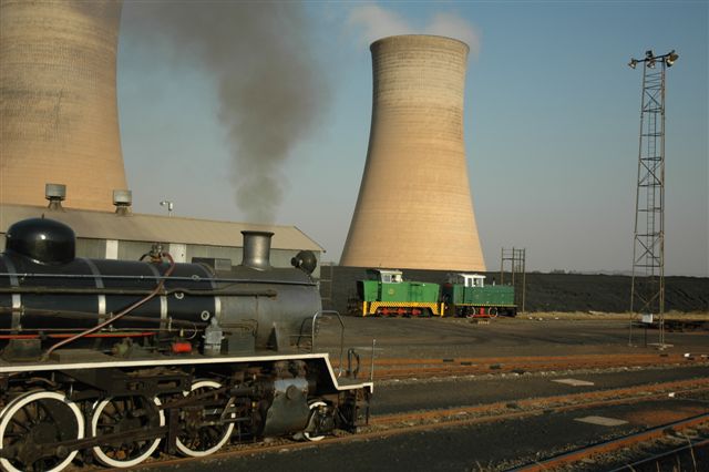Smokestacks and steam. Industrial scene at the Rooiwal Power station, when FOTR ran an excursion train to this interesting system. In the background are two of the company's shunt diesels, near to their shed. The huge cooling towers give an unusual perspective aspect.