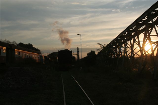 Sunset between the struts of the coalstage - coaches, locomotive and smoke highlighted..