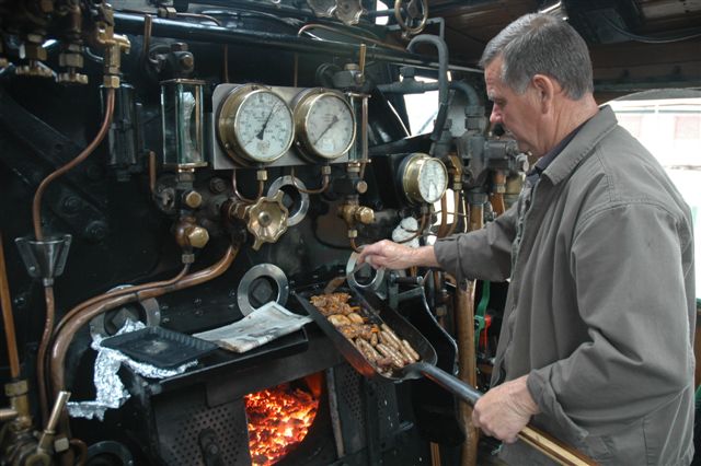 Tshwane Explorer activities. Friends of the Rail gourmet kitchen, in the cab of class 19D 2650. Driver Frik Boshoff grills up a delightful meal of sausage, wors and chicken kebabs, on the trusty shovel. Such forms of cooking are common practice on any steam locomotive!