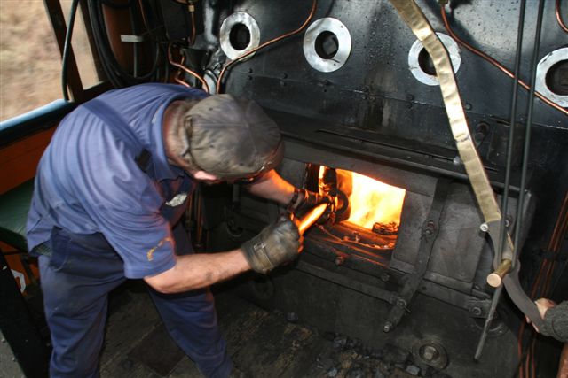 John feeds the furnace while Cliff keeps a hand on the regulator bar..